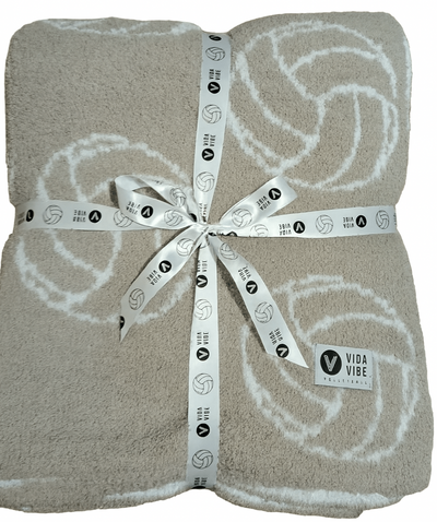 Folded beige blanket with white volleyball patterns and a ribbon, branded 'Vida Vibe'.